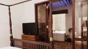 Une chambre à coucher avec un lit à baldaquin, un téléviseur posé sur un meuble en bois, et une vue sur la salle de bain à travers une porte en verre.
