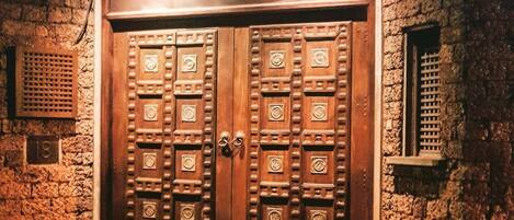 A large wooden double door with intricate carvings, set in a stone building with a brick-paved entrance.