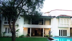 Une maison à deux étages avec une piscine, un patio couvert et un arbre dans le jardin.