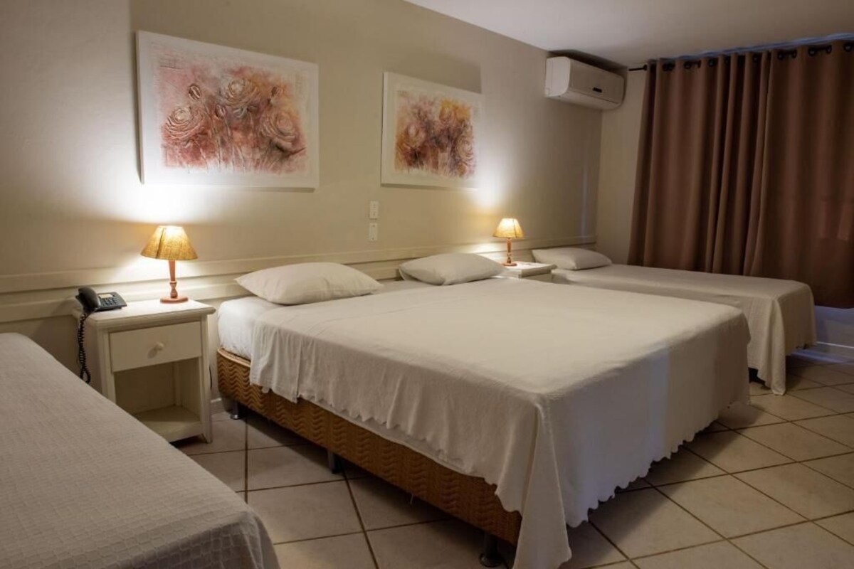 Habitación de hotel con dos camas, una mesita de noche con lámpara, un teléfono y cuadros en la pared.