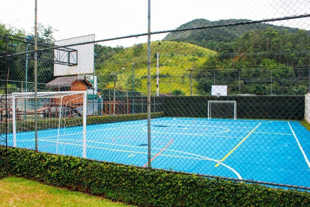Uma quadra de basquete ao ar livre cercada por uma grade, com um aro e um edifício ao fundo.
