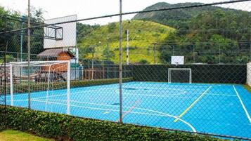 Uma quadra de basquete ao ar livre cercada por uma grade, com um aro e um edifício ao fundo.