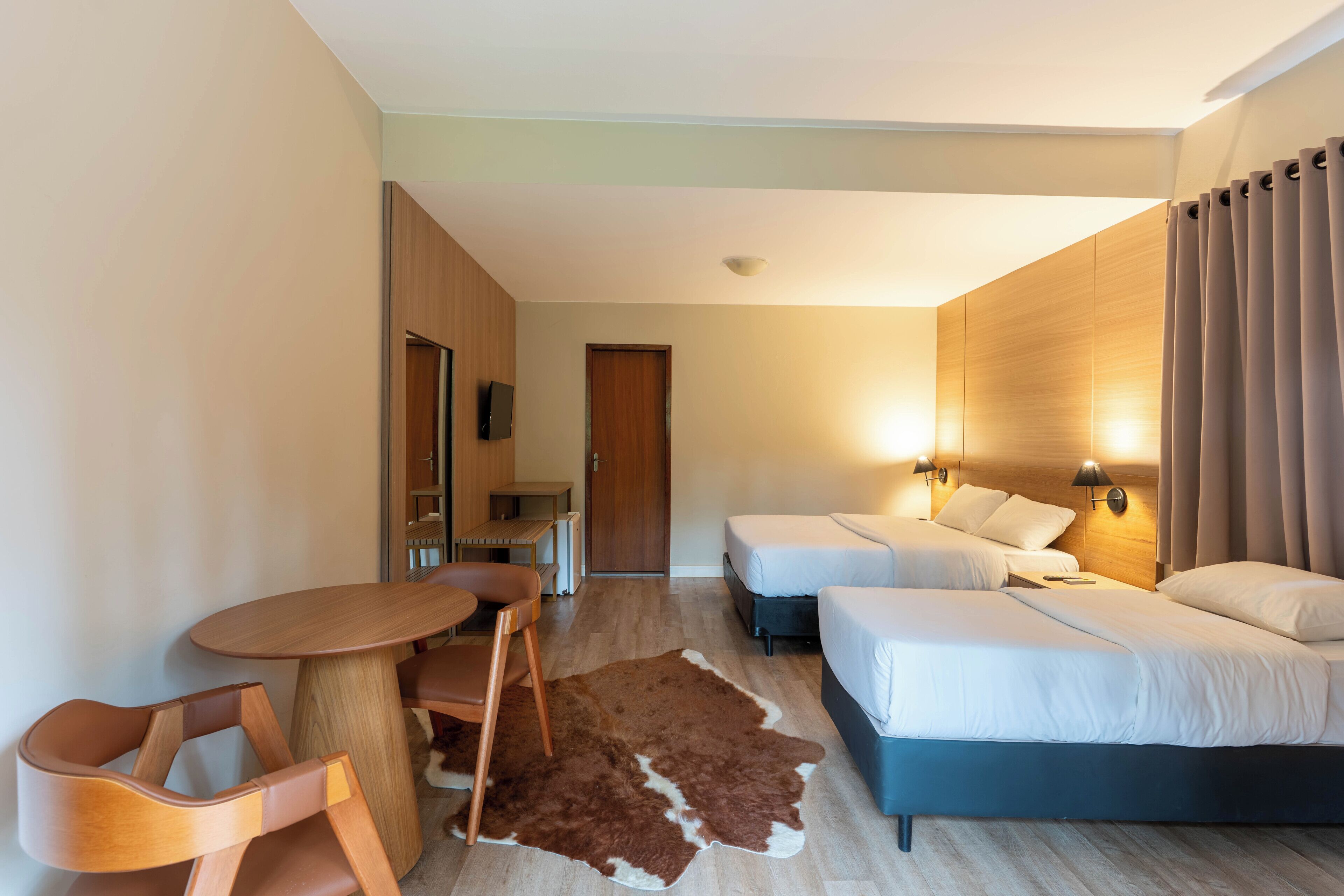 A hotel room with a bed, two bedside tables, a desk with a chair, a small table, and a cowhide rug.