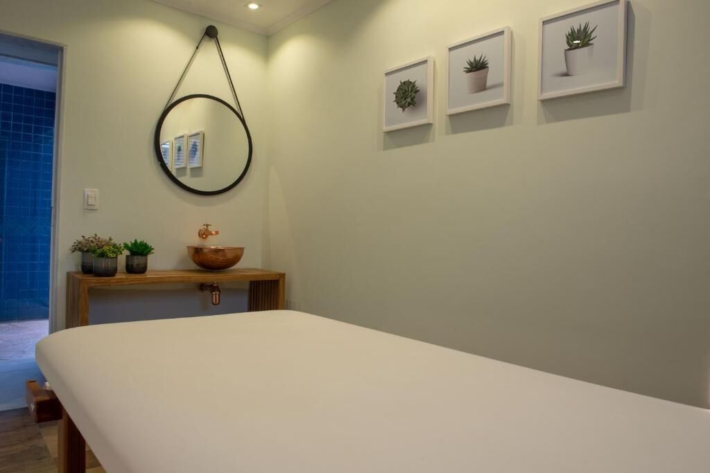 A minimalist bedroom with a large bed, a wooden bedside table with a bowl and potted plants, a round mirror, and framed pictures on the wall.