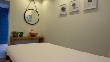 A minimalist bedroom with a large bed, a wooden bedside table with a bowl and potted plants, a round mirror, and framed pictures on the wall.