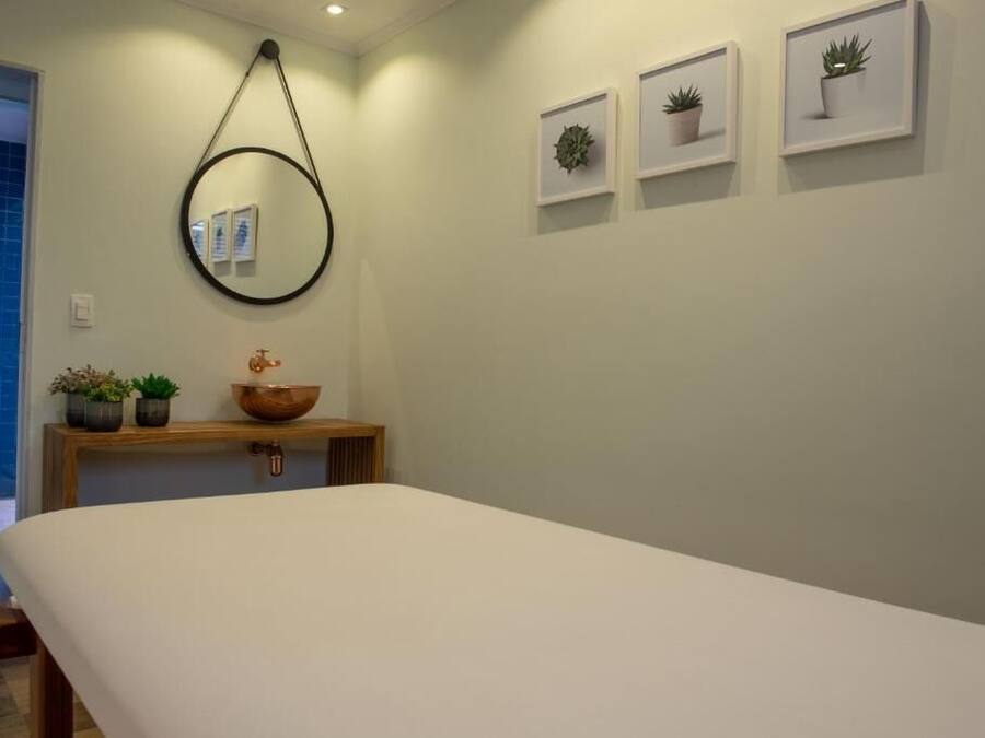 A minimalist bedroom with a large bed, a wooden bedside table with a bowl and potted plants, a round mirror, and framed pictures on the wall.
