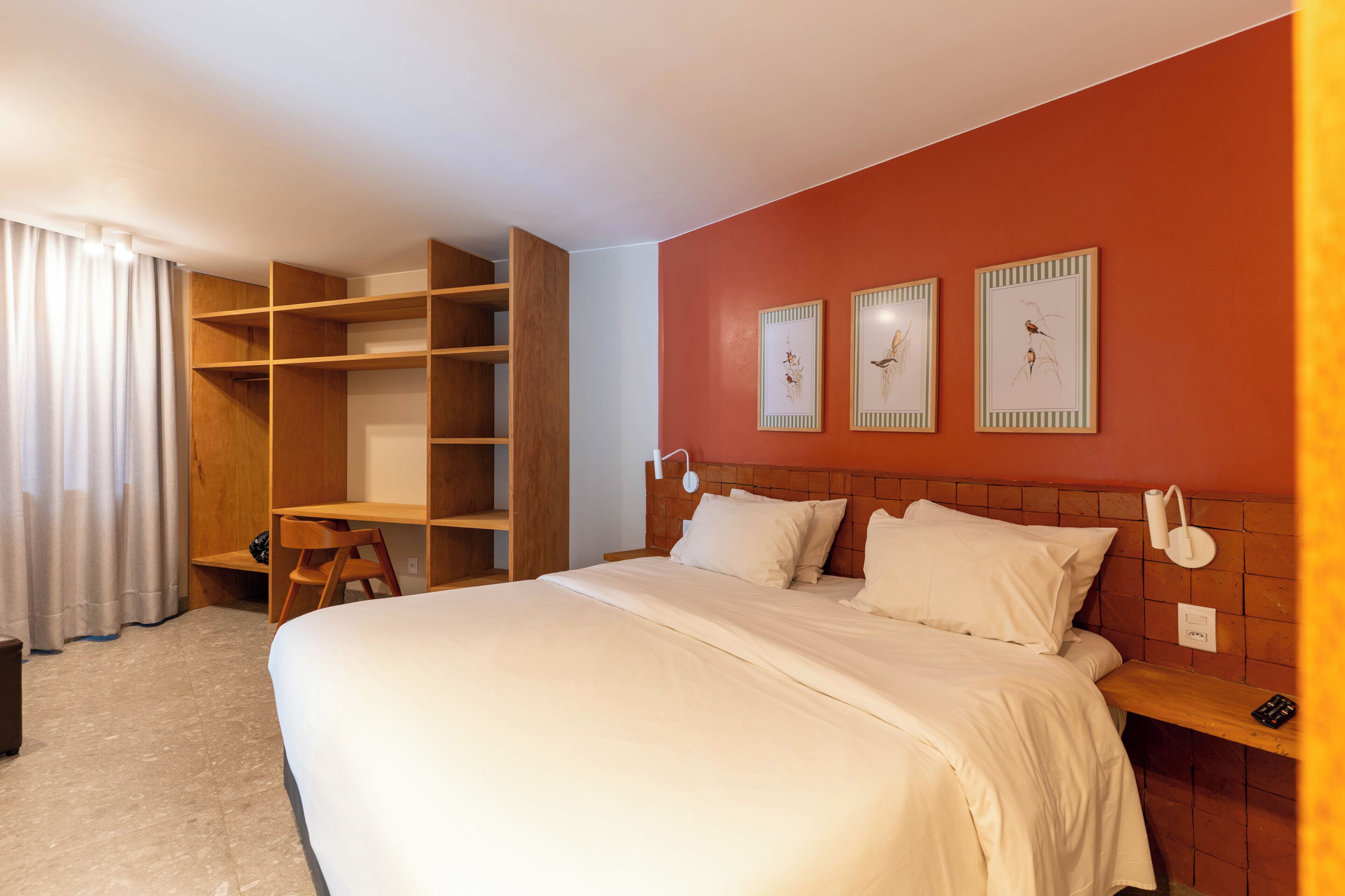 A hotel room with a large bed, wooden shelving, a desk, and artwork on the wall.