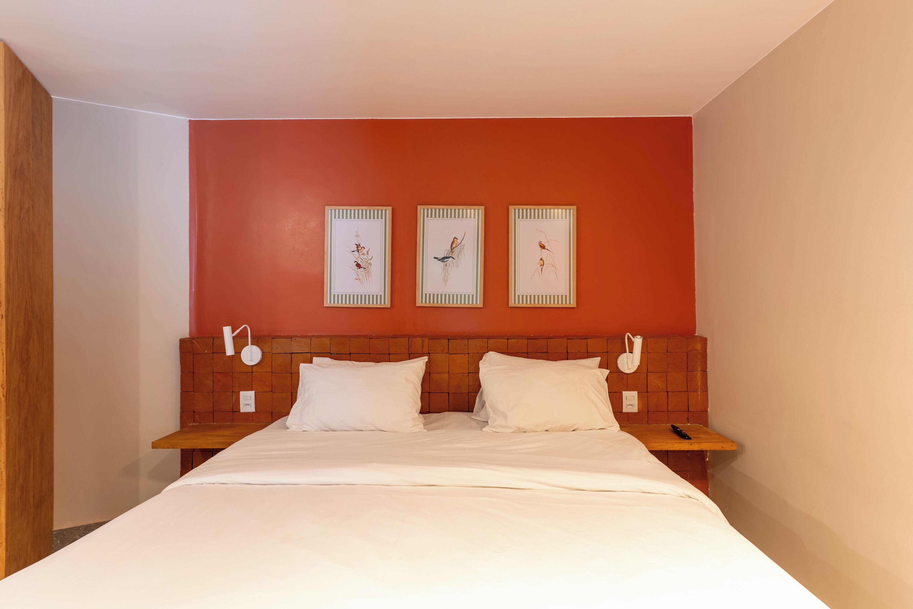 Habitación de hotel con cabecera de madera, ropa de cama blanca y tres cuadros en la pared.