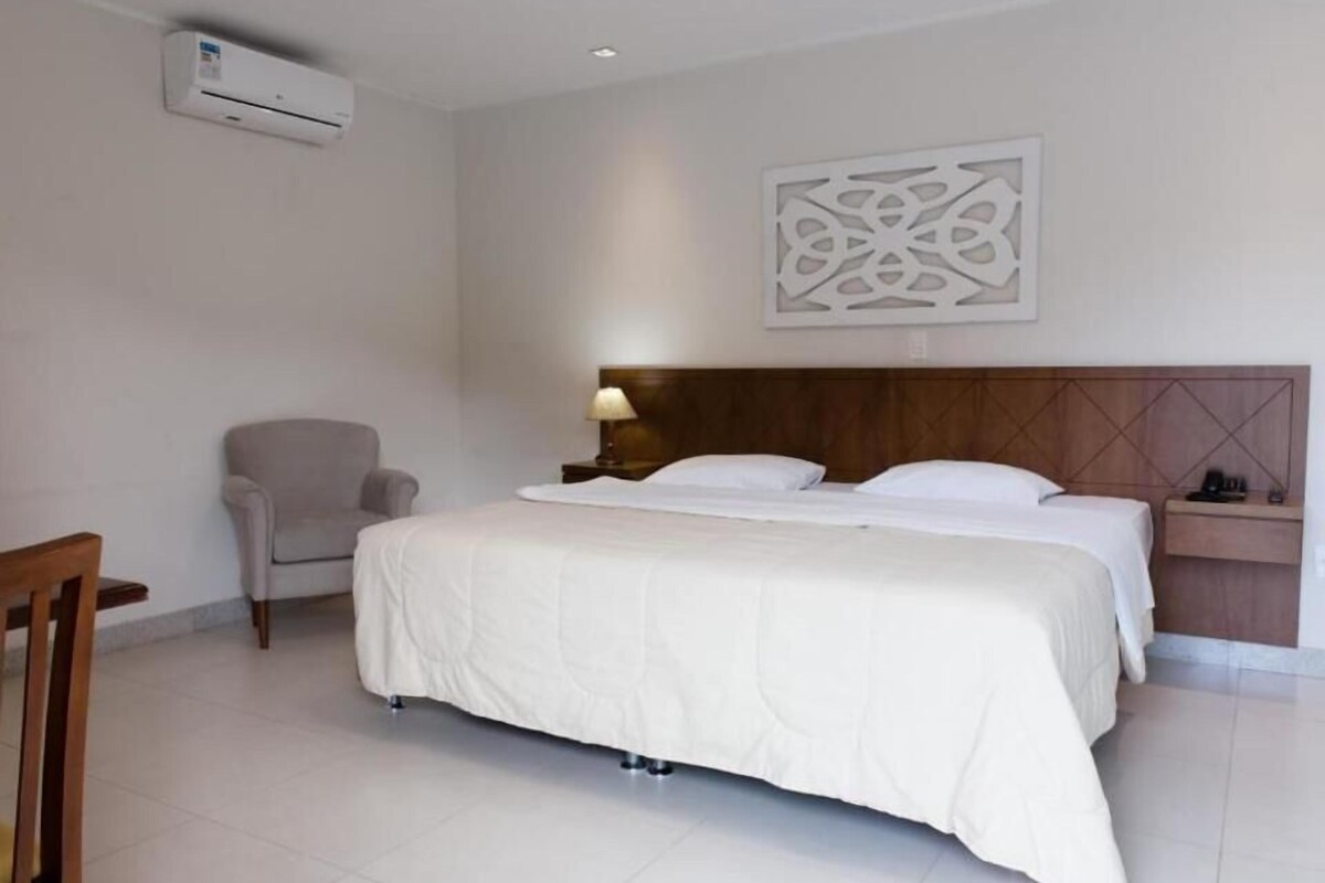 Una habitación de hotel con una cama, una silla, una mesita de noche y un aire acondicionado de pared.