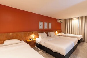 Habitación de hotel con una cama grande, dos mesitas de noche, aire acondicionado de pared y una ventana con cortinas.