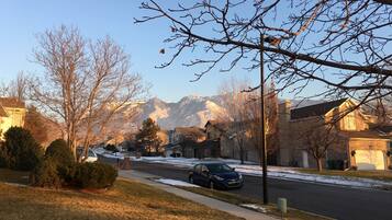 A residential street with houses, a parked car, and mountains in the background.