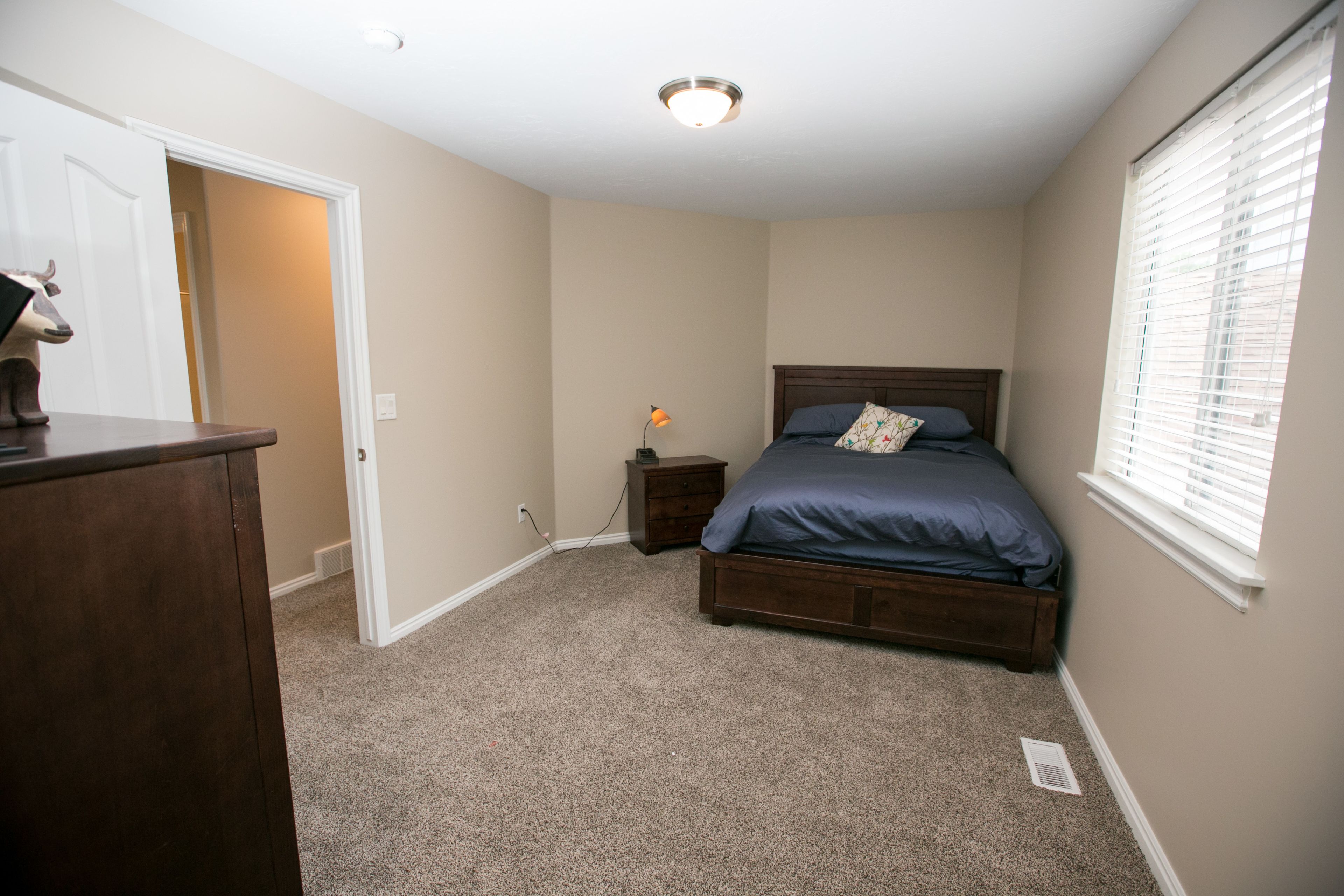 A bedroom with a bed, nightstand, dresser, and a door leading to another room.