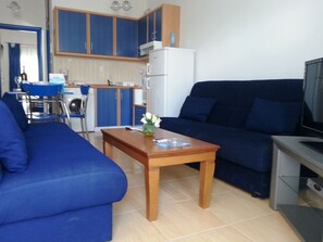 Una sala de estar con un sofá azul, una mesa de centro de madera y un televisor.