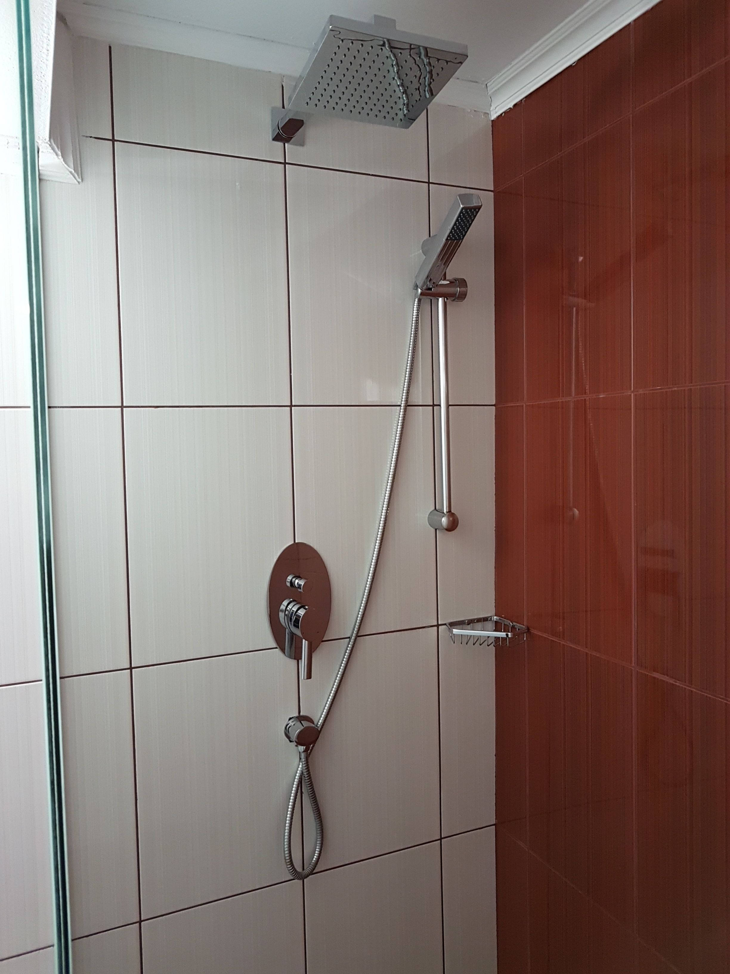 A shower with a handheld showerhead and a wall-mounted control panel.