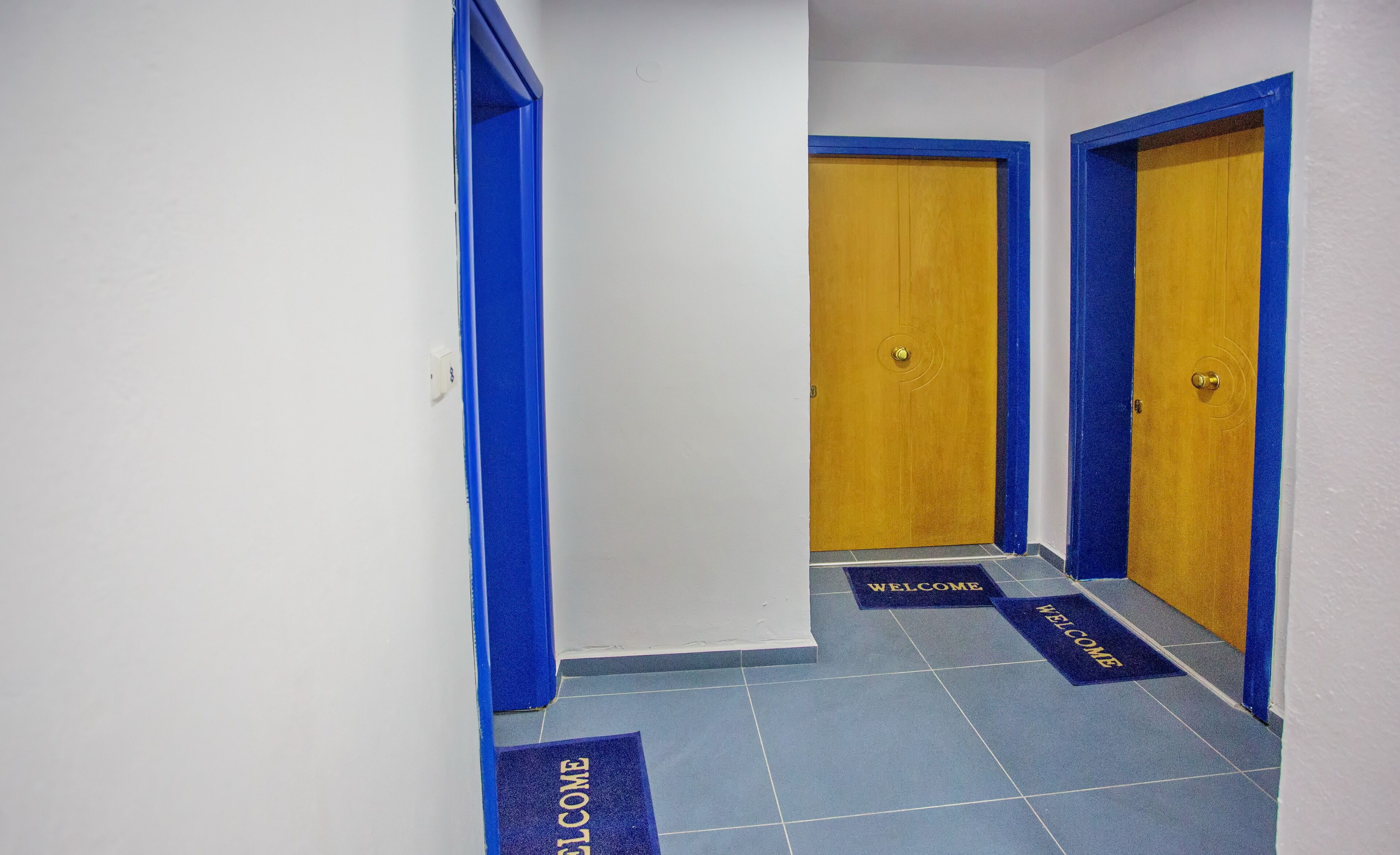 A hallway with blue-framed doors and blue welcome mats on the floor.