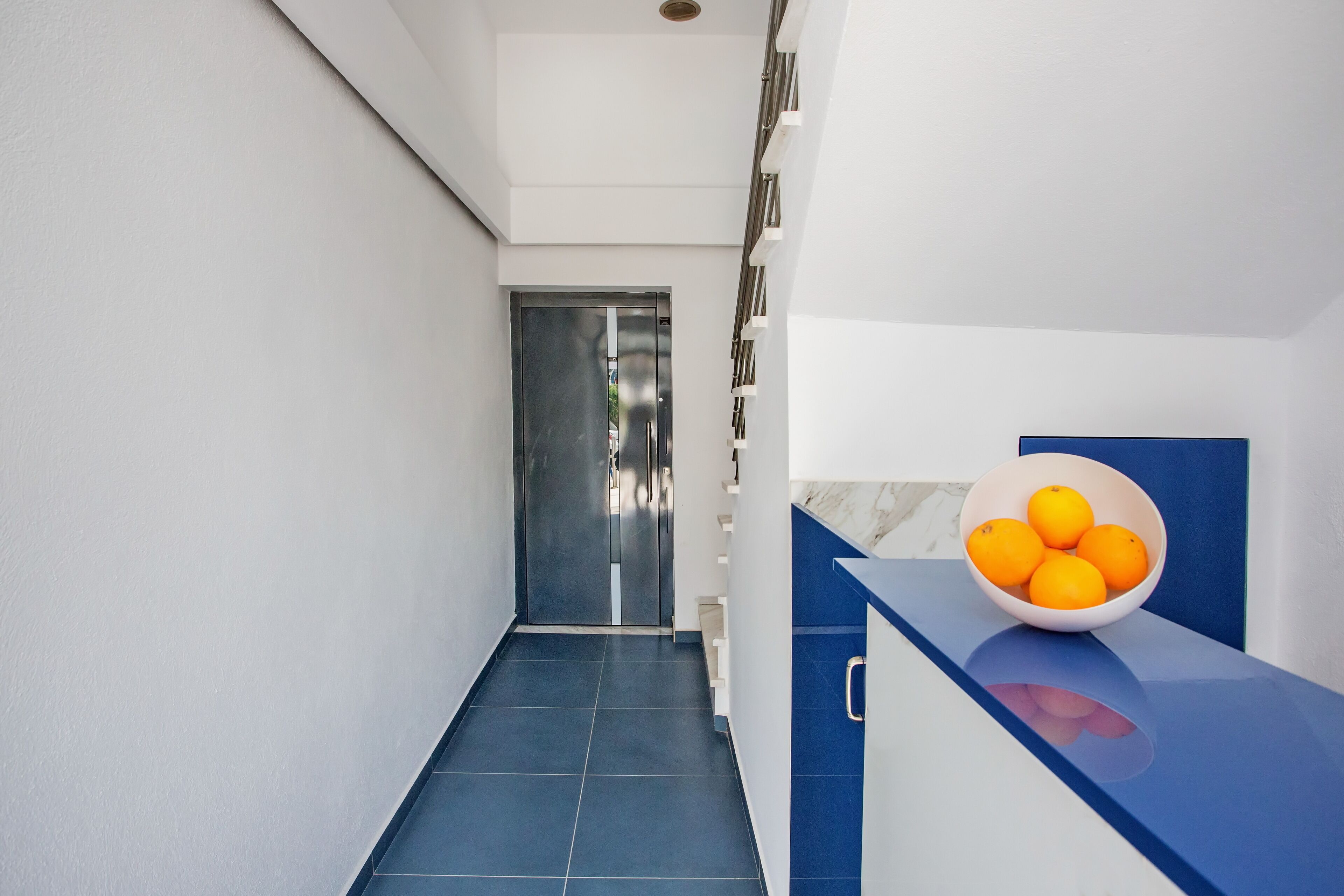 A modern hallway with a blue counter and a bowl of oranges.