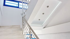 A modern staircase with a metal railing, white walls, and a skylight. - The Blue Apartments and Beach (Pangaio)