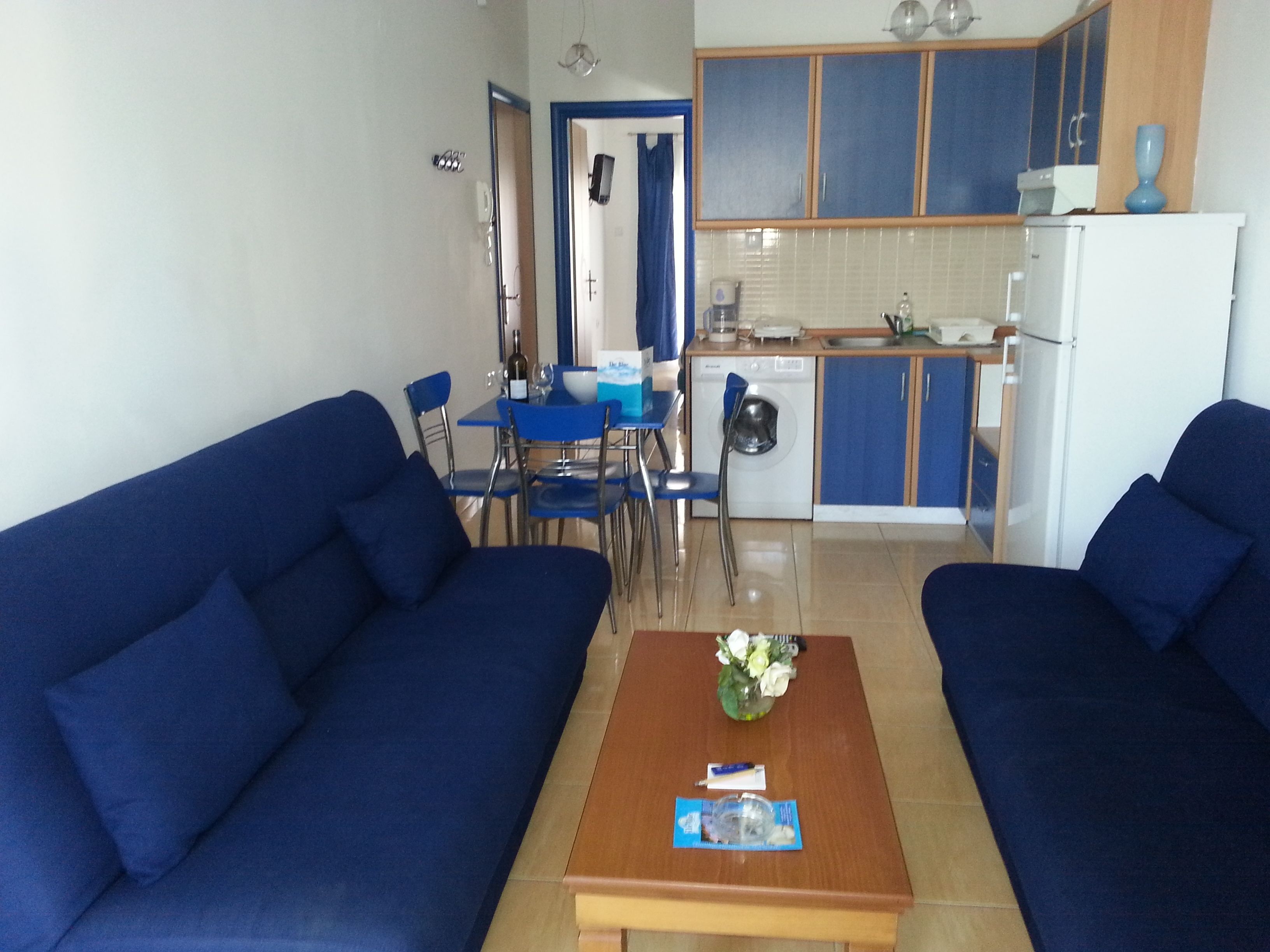 Una sala de estar con dos sofás azules, una mesa de centro de madera y un comedor con sillas y una mesa azules.