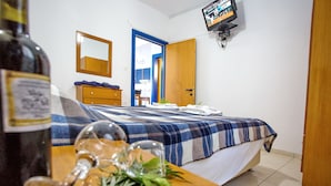 A bedroom with a bed, a wooden wardrobe, a television mounted on the wall, and a bottle of wine on a table. - The Blue Apartments and Beach (Pangaio)