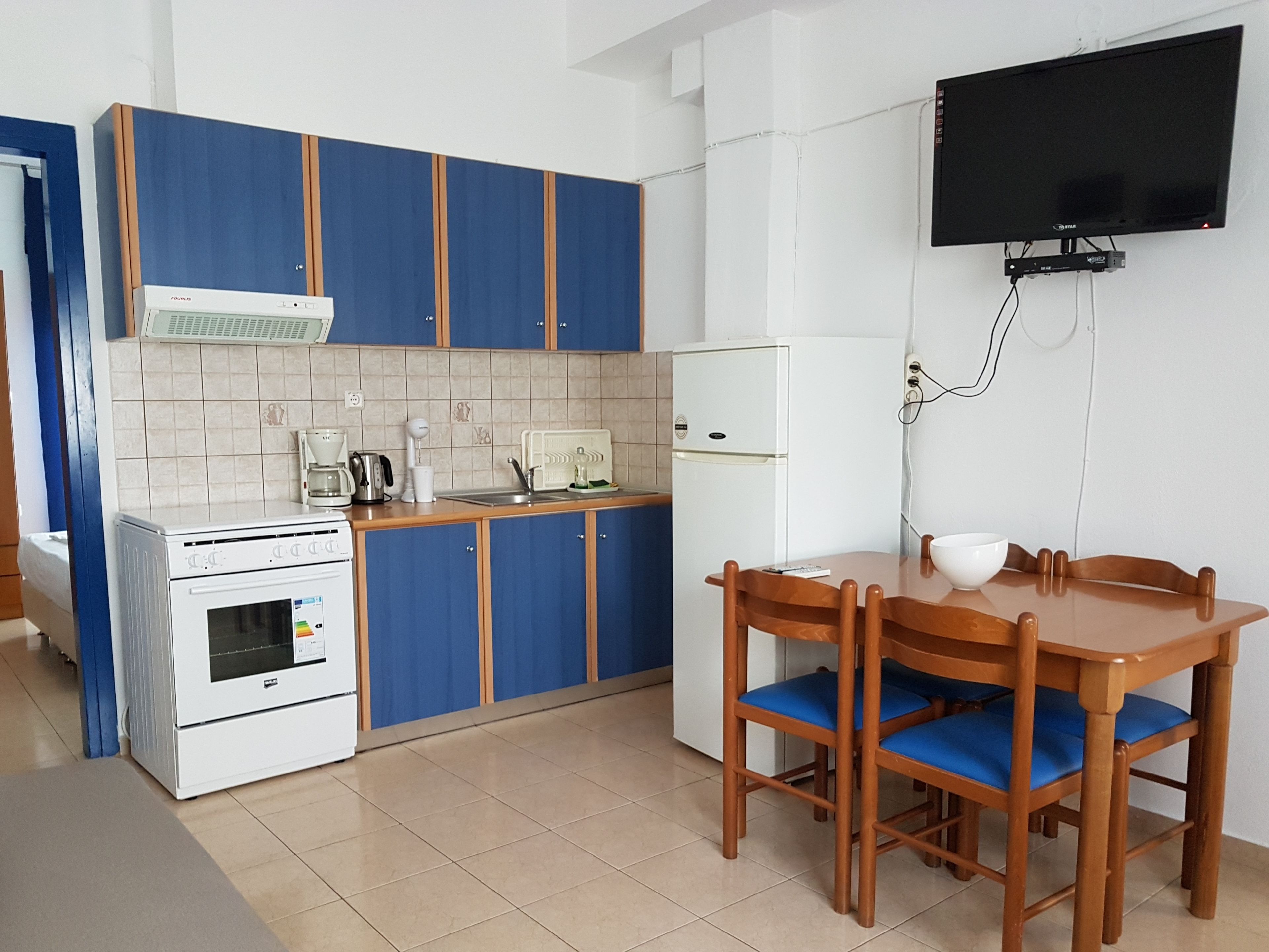 Una cocina compacta con armarios azules, un refrigerador blanco, una estufa y una mesa de comedor con sillas.