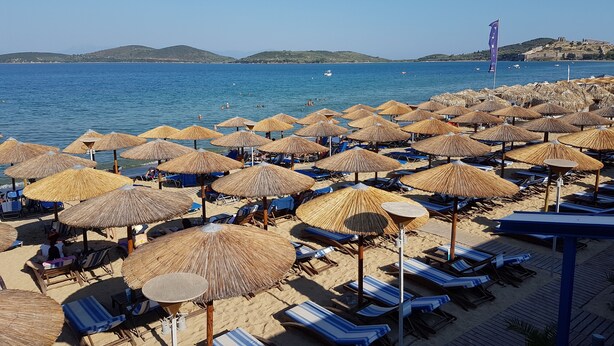A beach with numerous straw umbrellas and lounge chairs, a clear blue sea, and distant hills. - The Blue Apartments and Beach (Pangaio)