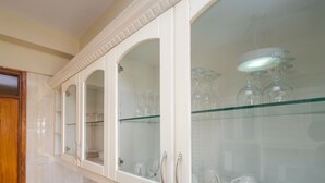 A kitchen with white cabinets, glass shelves, and a wooden door. - KenGen Furnished and Serviced Apartments (Nairobi)