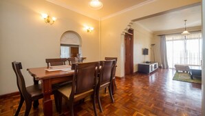 A dining area with a wooden table and chairs, a chandelier, and wall sconces. - KenGen Furnished and Serviced Apartments (Nairobi)