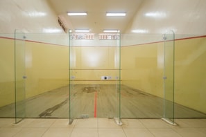 A squash court with glass walls, a wooden floor, and a red line marking the playing area.