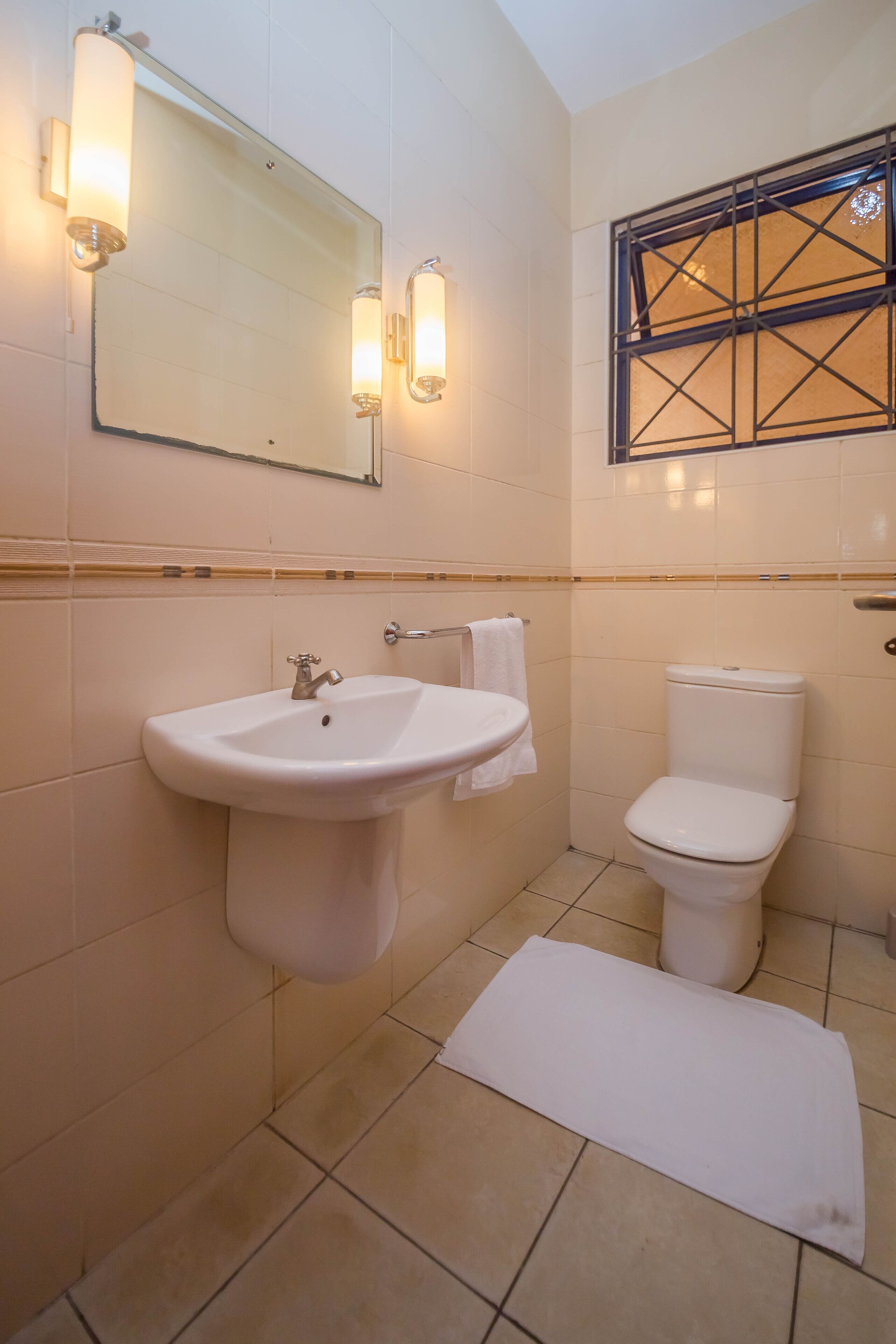 Ein Badezimmer mit Waschbecken, Toilette und einem Fenster mit dekorativem Gitter.