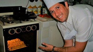 A chef in a white uniform and hat standing next to an oven with a tray of food inside. - Villa Cristal Holguin (Holguín)