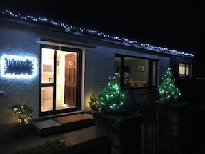A house with a lit sign, a door, and two Christmas trees.