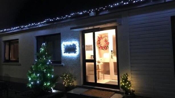 A house with a lit sign, a wreath, and two Christmas trees. - Millview Bed & Breakfast (Ullapool)