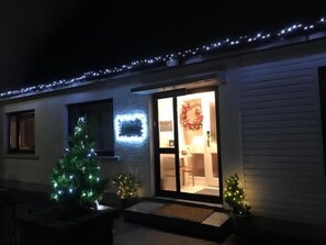 A house with a lit sign, a wreath, and two Christmas trees. - Millview Bed & Breakfast (Ullapool)