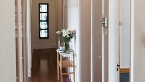 A hallway with a wooden chair, a small table with a vase of flowers, and a window with multiple panes. - Millview Bed & Breakfast (Ullapool)