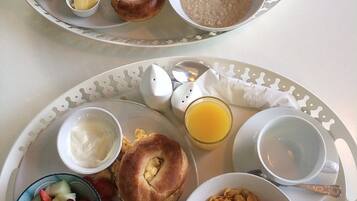 A breakfast tray with bagels, cream cheese, orange juice, and cereal.