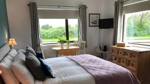 A bedroom with a bed, a desk, a chair, a TV, and a window with curtains. - Millview Bed & Breakfast (Ullapool)