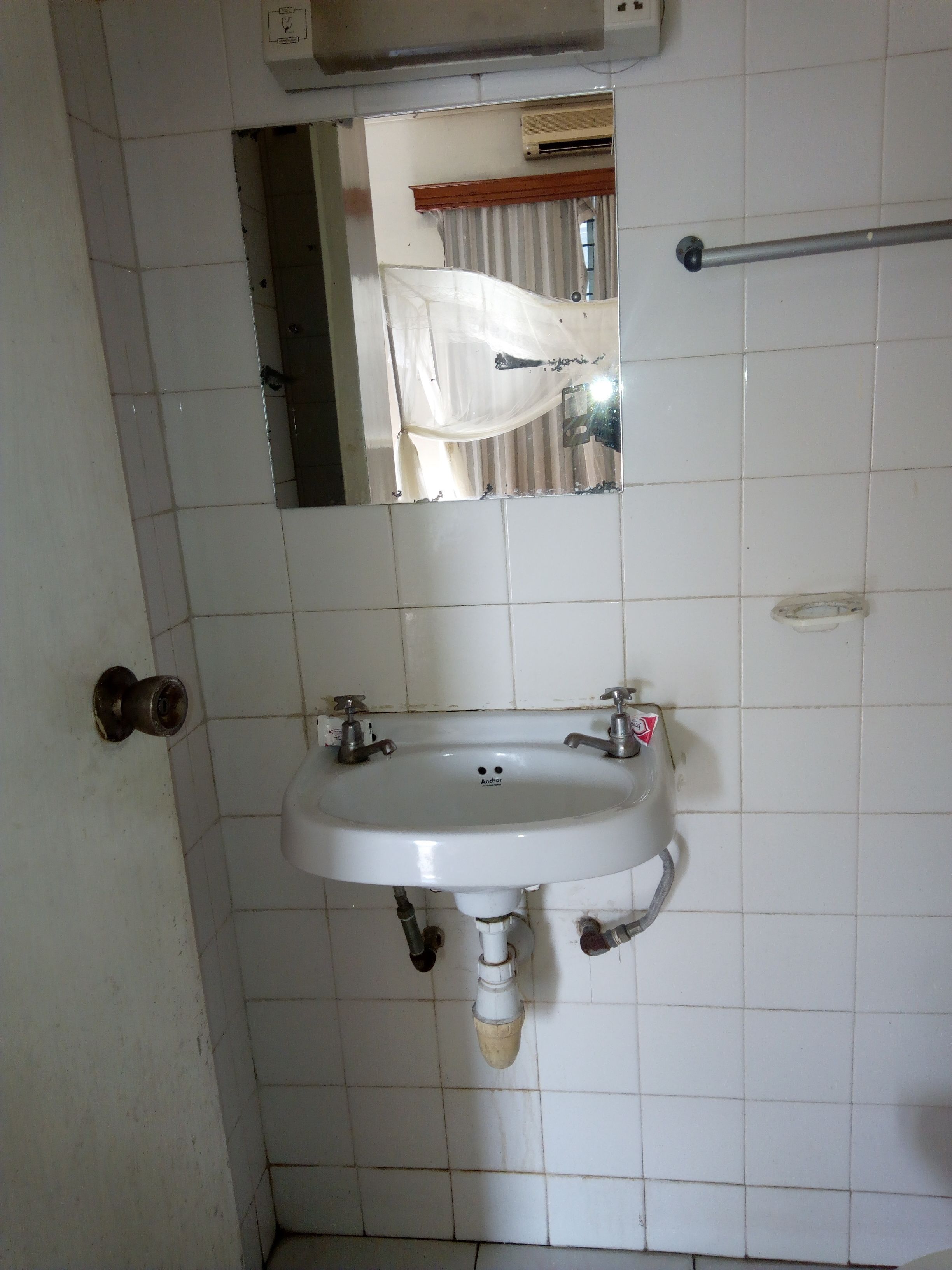 Un baño con un lavamanos blanco, un espejo encima y un perchero a la derecha.