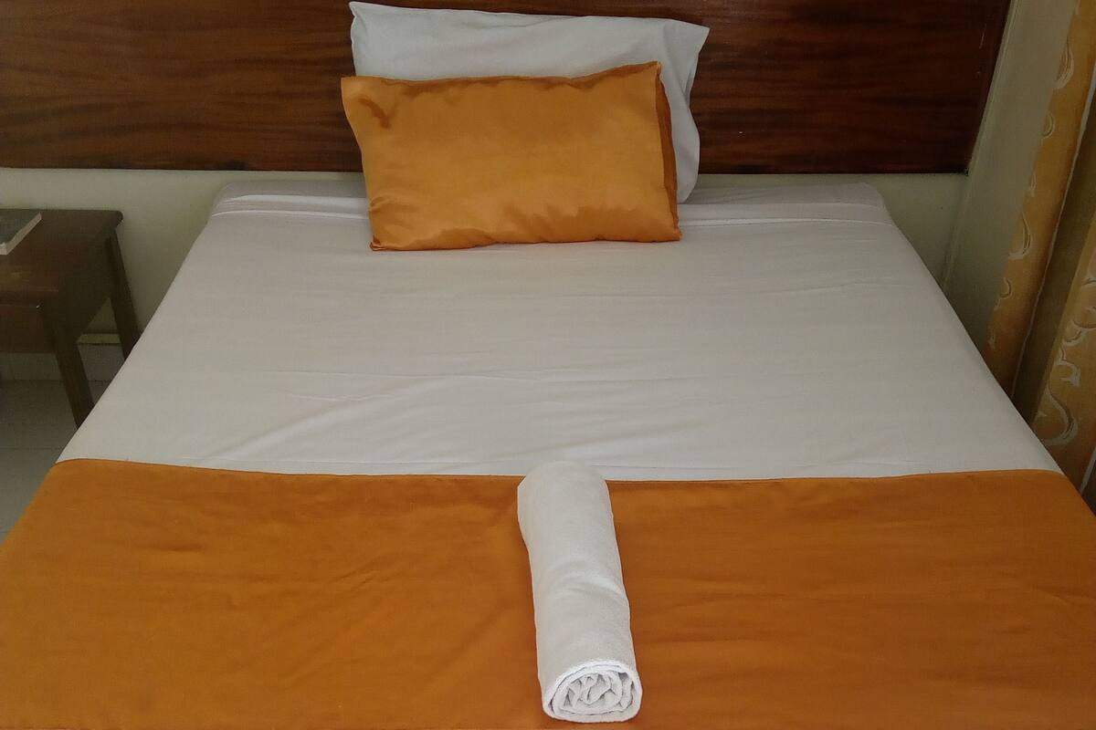Una cama bien hecha con ropa de cama blanca y naranja, un cabecero de madera y una mesita de noche pequeña.