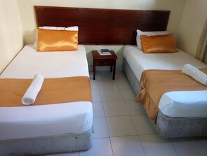 A hotel room with two single beds, each with a wooden headboard, white linens, and orange pillows. There is a small wooden nightstand between the beds. - Hotel Dorse (Mombasa)