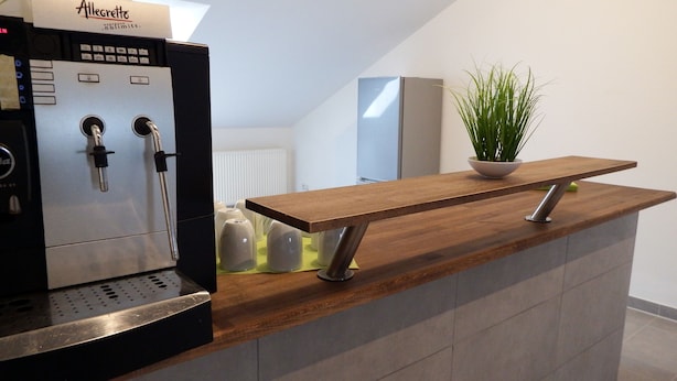 A modern kitchen with a built-in espresso machine, a wooden countertop, and a potted plant. - Hotel Radau (Bad Harzburg)