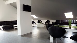 A modern living room with a sectional sofa, two black chairs, a coffee table, and a flat-screen TV mounted on the wall. - Hotel Radau (Bad Harzburg)