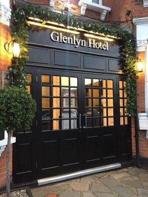 The exterior of the Glenlyn Hotel with a black entrance door, a sign above the door, and a small tree to the left. - Glenlyn Apartments (London)