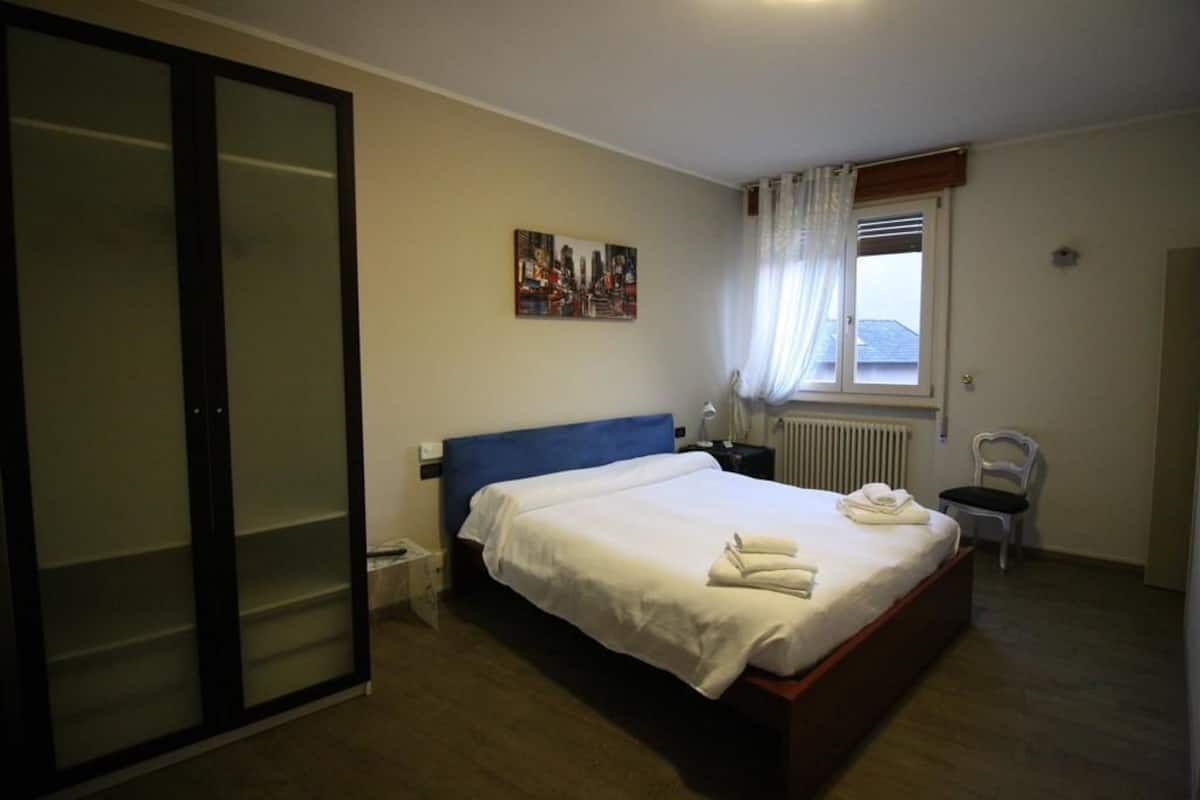 Une chambre à coucher avec un lit, une chaise, un radiateur, une fenêtre avec des rideaux et un tableau au mur.