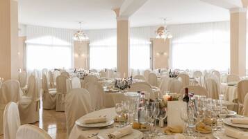 Una sala da banchetti con tavoli rotondi apparecchiati per un evento formale, ognuno con tovaglioli piegati, bicchieri da vino e bottiglie.