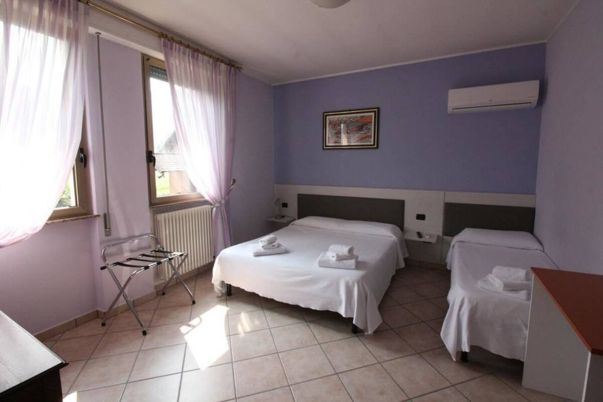 Une chambre d’hôtel avec deux lits, un radiateur, une fenêtre avec des rideaux et un tableau au mur.