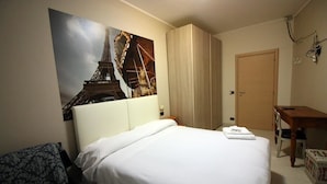 Et hotelværelse med en seng, et skrivebord, en stol og et billede af Eiffeltårnet.