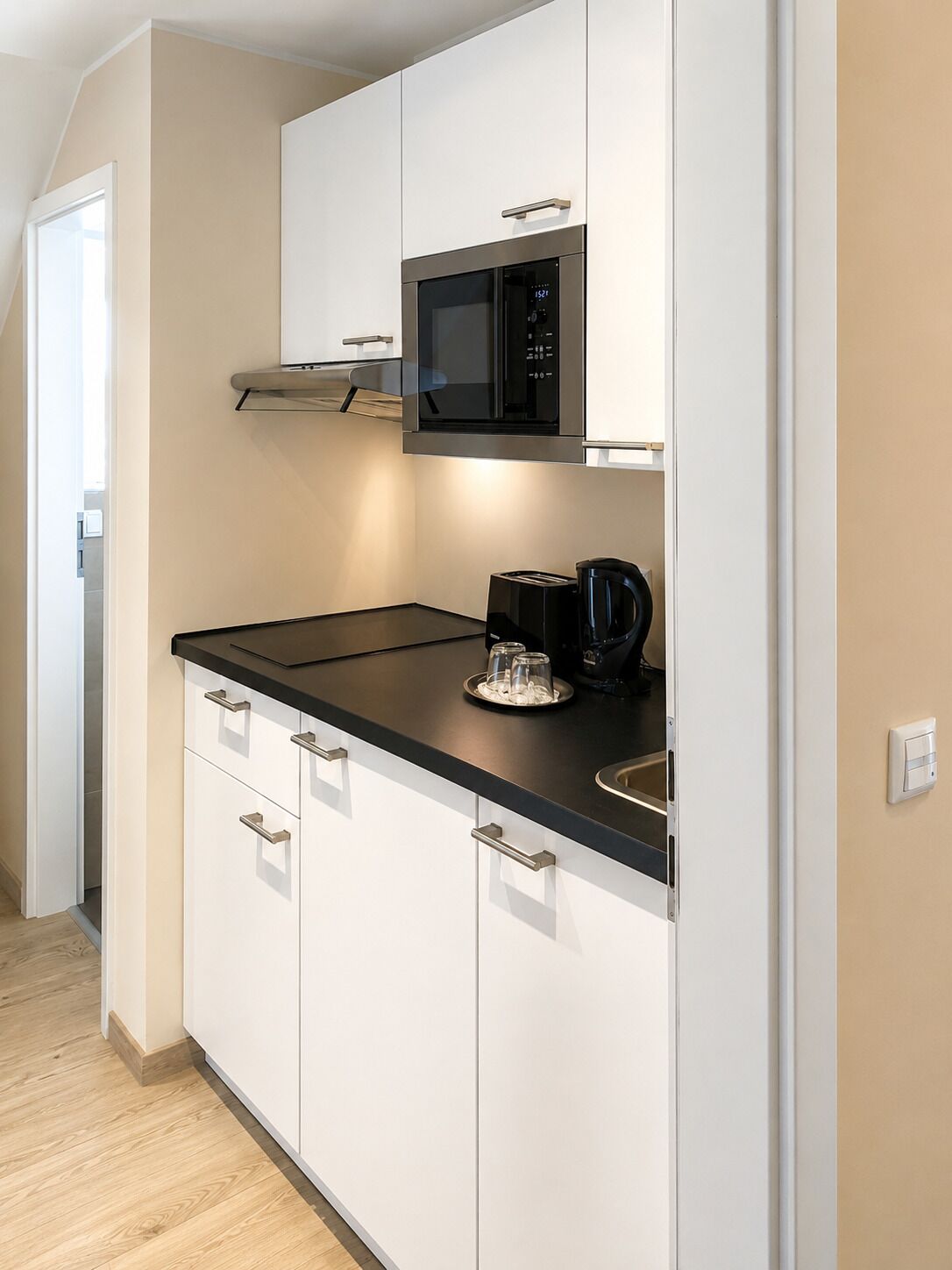 Een moderne keuken met witte kasten, een zwart aanrecht, een magnetron en een koffiezetapparaat.
