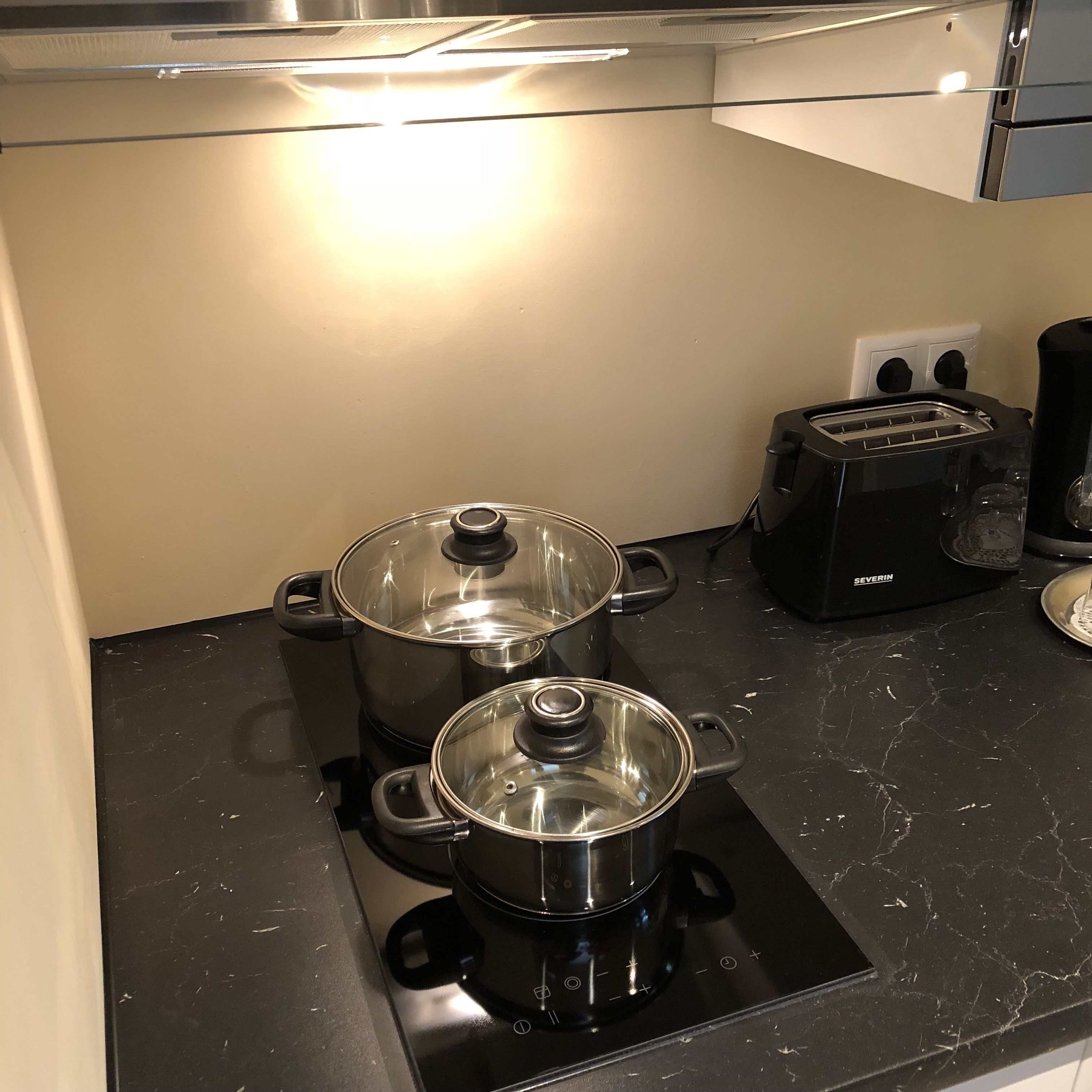 Une cuisine équipée d’une cuisinière, de deux casseroles, d’un grille-pain et d’une machine à café.