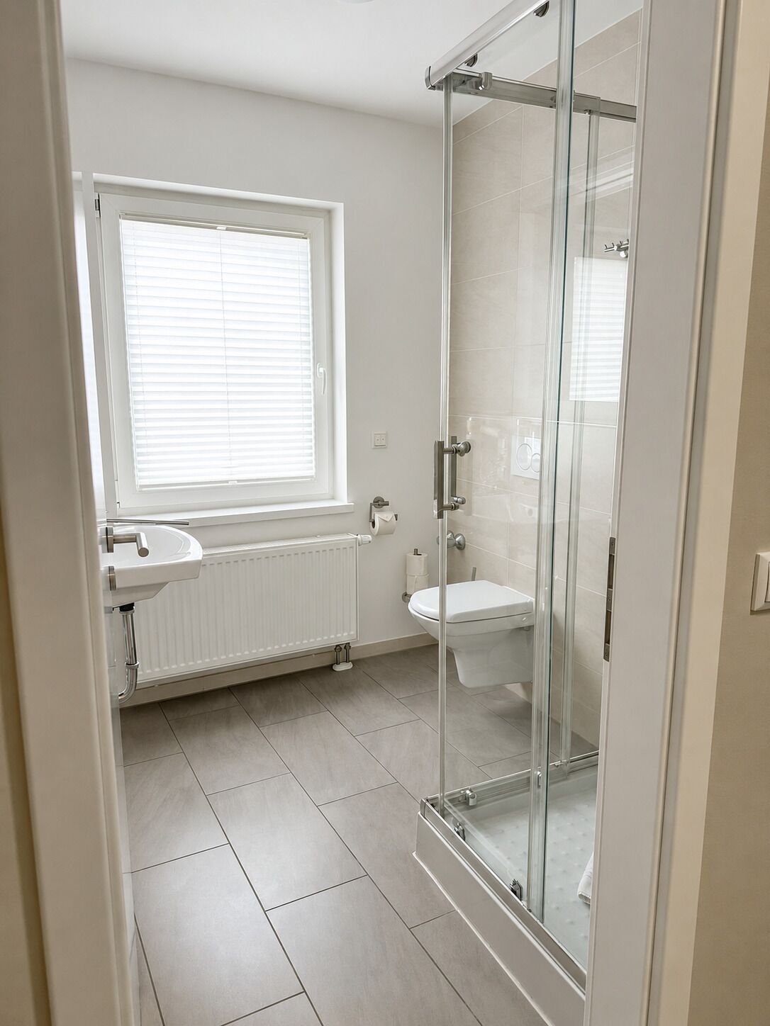 Une salle de bain avec une douche à parois de verre, des toilettes, un lavabo et une fenêtre avec des stores.