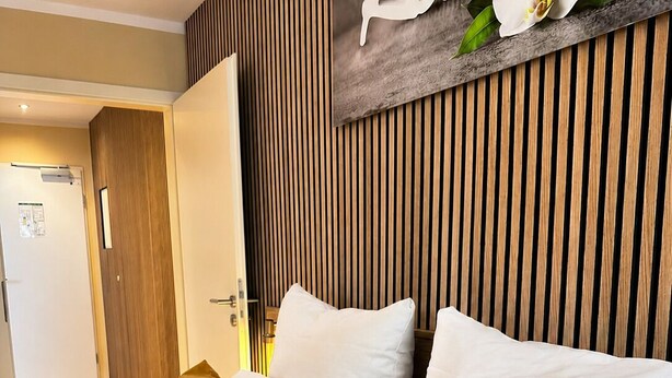 A hotel room with a bed, pillows, a wooden slat wall, and a sign with the word 'Relax'. - Hotel Select Suites & Aparts (Moenchengladbach)